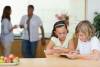 Children using tablet in the kitchen with parents behind them